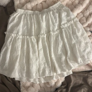 Vit volangkjol  - Supersöt vit kortkjol med volanger och elastisk midja. Kjolen har broderade spetsdetaljer. 