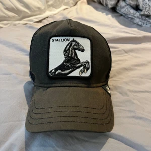 Svart keps Goorin Bros Stallion - Svart truckerkeps från Goorin Bros med broderad patch framtill med en svart häst och texten 'Stallion'. Kepsen har justerbar snapback och mesh baktill för extra ventilation. Perfekt accessoar för en cool och sportig look.