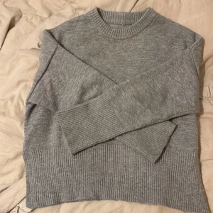 Grå stickad tröja med slits från pull & bear - Mysig grå stickad tröja med bred ribbad kant nertill och vid ärmslut. Tröjan har rund halsringning och en snygg slits i sidan som ger en extra detalj. Perfekt för lager-på-lager och chill dagar.
