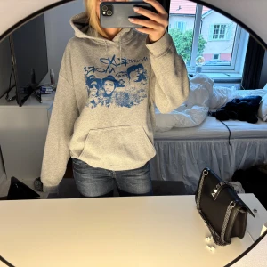 Grå hoodie med blått tryck Mount Rap More - Säljer en grå hoodie med blått grafiskt tryck på bröstet och texten 'Mount Rap More'. Tröjan har huva med snörning och en stor magficka. Materialet är bomull och polyester.