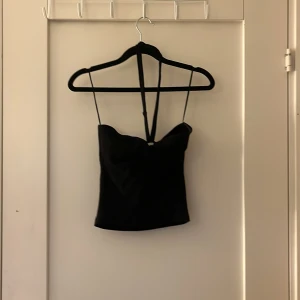 Svart korsett-topp från Gina Tricot - Säljer en svart korsett-topp från Gina Tricot i storlek S. Toppen har smala axelband och en snygg croppad passform med lätt v-ringad front. Perfekt för dig som gillar stilrena och trendiga plagg med en enkel men edgy vibe.
