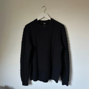 Mörkblå stickad tröja från Uniqlo L - Mörkblå kabelstickad tröja från Uniqlo i storlek L. Tröjan har rund halsringning, ribbade muddar och är tillverkad i en mix av akryl, polyester, ull och nylon. Perfekt för lager-på-lager och en clean look till höst och vinter. 4F2