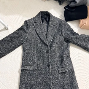 Grå rutig kappa med knappar - Snygg grå kappa med klassiskt rutig mönster och två svarta knappar framtill. Jackan har breda slag, två fickor med lock och är helfodrad. Perfekt för dig som gillar stilrena och tidlösa plagg med lite edge.