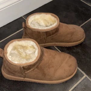 Bruna boots med fuskpälsfoder - Mysiga bruna vinter boots ( fejk Uggs) med rund tå och platt sula, fodrade med mjuk fuskpäls på insidan. Utsidan är i mockaliknande material och har en enkel design utan snörning eller dragkedja. Perfekta för kalla dagar när du vill hålla dig varm. I storlek 37💕