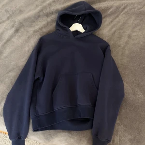 Mörkblå hoodie från Gina Tricot - Mörkblå hoodie från Gina Tricot. Tröjan har huva, magficka och ribbade muddar. Tillverkad i 70% bomull och 30% polyester för en mjuk och skön känsla. Perfekt för chill dagar eller när du vill ha en enkel och stilren look.