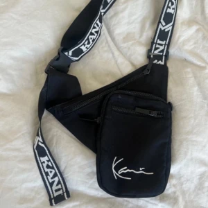 Karl Kani Väska 🖤 - Svart axelremsväska med justerbar rem med KANI logga. Väskan har två fack med dragkedja och en stilren KANI signatur 🖤