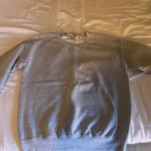 Grå sweatshirt Byherinian med tryck - Grå sweatshirt från Byherinian med stort svart tryck på ryggen som föreställer en ängel och text. Tröjan har rund hals, långa ärmar och ribbade muddar vid ärmslut och nederkant. Perfekt för dig som gillar streetwear och snygga detaljer.