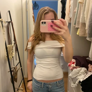 Vit offshoulder topp Zara - Säljer en vit offshoulder topp med bred kant upptill. Sitter tight och har en stilren, enkel look. Perfekt till jeans eller kjol och passar dig som gillar en clean och fräsch stil. Materialet är mjukt och stretchigt bomullstyg.