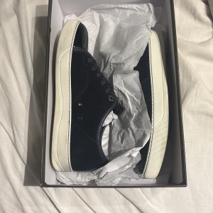 Blå lanvins - Snygga mörkblå sneakers med vit platt sula och snörning. Ovandelen är i mocka och har en glansig, lackad tå i svart som ger en cool kontrast. Metallöglor och stilren design gör dem perfekta för dig som gillar en clean look. Passar dig som vill ha något unikt i skogarderoben. Uk 5 passar 41-42 skulle jag säga 