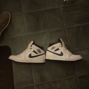 Nike Air Jordan 1 Mid vit/svart - Säljer ett par Nike Air Jordan 1 Mid i klassisk vit och svart färg. Skorna har svart swoosh, vita paneler och svarta detaljer kring kragen Använda 1 gång. 