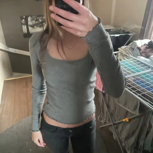 Grå ribbad långärmad topp Gina Tricot - Säljer en grå ribbad långärmad topp från Gina Tricot i storlek XS. Toppen har croppad passform, rundad halsringning och söta volangdetaljer vid ärmslut och nederkant. 