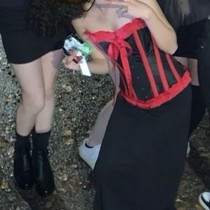 Svart och röd korsett från Burleska - Säljer en snygg korsett från Burleska i svart med röda detaljer. Den har snörning i ryggen, knappar framtill och en rosett vid bysten. Som ny kostar den ungefär 1100-1200kr 