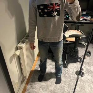 Stickad tröja med tryck - Snygg grå stickad tröja med Australien-flagga på bröstet. Tröjan har ribbade muddar och nederkant samt mörka armbågslappar som cool detalj. Perfekt för dig som vill sticka ut lite extra och gillar unika plagg. Tveka inte på att ställa frågor om du har några!! Priset är inte skrivit i sten då våga buda!!