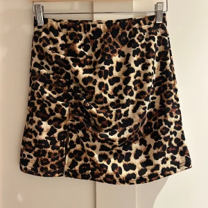 Leopardmönstrad kortkjol från SHEIN - Säljer en snygg kortkjol från SHEIN med leopardmönster i beige, svart och bruna toner. Kjolen har en rak form och är gjord i ett mjukt syntetmaterial. Perfekt för dig som vill sticka ut med ett djuriskt print och cool vibe.