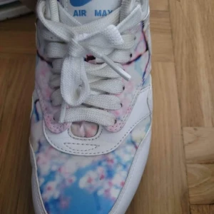Nike Air Max med blommigt mönster - Nike Air Max sneakers med unikt blommigt mönster i rosa, blått och vitt. Skorna har vit snörning, rund tå och platt sula. Ovandelen är i syntet och skinn, med klassisk Air Max-dämpning och vit swoosh på sidan. Perfekt för dig som vill sticka ut med färg och stil.