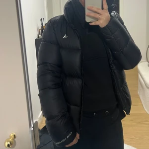 Svart pufferjacka från Calvin Klein Jeans - Svart pufferjacka från Calvin Klein Jeans med stor logga på insidan och liten logga på ärmen. Jackan har hög krage, dragkedja och quiltad design. Perfekt för kalla dagar och har en clean, modern look som funkar till streetwear. Den är knappt använd.