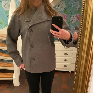 Grå skepparkavaj med bred krage - Säljer en stilren grå skepparkavaj med bred krage. Jackan har en rak och loose passform med långa ärmar och stora knappar. Perfekt för dig som gillar klassisk och enkel design med lite edge. Storlek 158-164 men skulle säga att det passar som xs💕