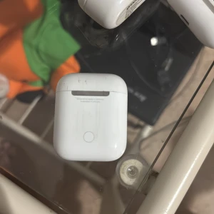 AirPods 2 - Apple AirPods 2 med laddningsetui. Trådlösa hörlurar med smidig anslutning till iPhone och andra Apple-enheter. Etuiet har synliga repor och mindre slitage, men hörlurarna ser ut att vara i gott skick. Perfekt för musik, samtal och träning.