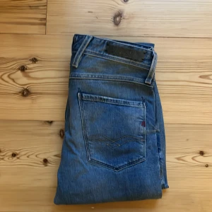 Blå Replay Anbass jeans - Säljer ett par blå Replay Anbass jeans med snyggt slitna detaljer och klassisk femficksdesign. Jeansen har slim passform. Perfekta för dig som gillar en avslappnad men stilren look.