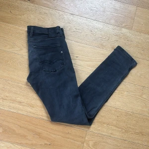  Replay Anbass Jeans - Svarta jeans från Replay i modellen Anbass som är Slimfit, storlek 32/32. Klassisk femficksdesign med dragkedja och knapp framtill. Jeansen har en stilren look och är tillverkade i ett mjukt och stretchigt bomullsmaterial för skön passform.
