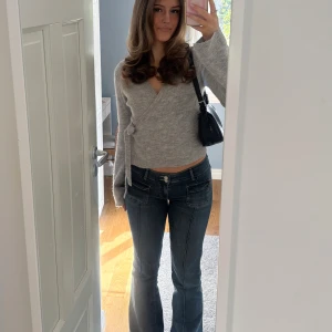 Grå omlottkofta - Säljer en stilren grå omlottkofta som är väldigt populär från Gina med knytband i midjan. Koftan har långa ärmar och är perfekt för en mysig och elegant look.