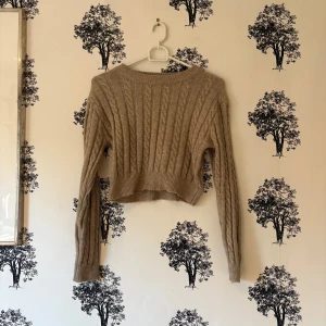 Beige croppad stickad tröja Shein - Säljer en beige croppad stickad tröja från Shein med kabelstickat mönster. Tröjan har lång ärm, rund hals och ribbade muddar vid ärmslut och nederkant. Perfekt för dig som gillar en chill och trendig look.