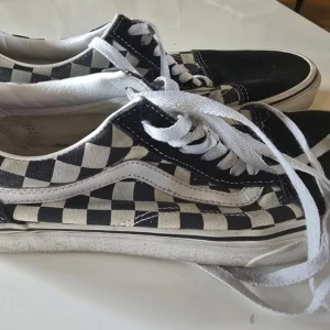 Vans Old Skool checkerboard sneakers - Klassiska Vans Old Skool sneakers med schackrutigt mönster. Perfekt för vardagsbruk eller skateboarding. Bekväma och stilrena.  Klassiska Vans Old Skool sneakers med svart mocka framtill och schackrutigt mönster på sidorna. Perfekt för en avslappnad och stilfull look. Bekväma skor som passar till många olika outfits.