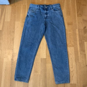Blå jeans från LMTD i rak modell - Snygga blå jeans från LMTD i klassisk rak modell. Jeansen har 4 fickor, bälteshällor och stängs med knapp och dragkedja. Materialet är robust denim i bomull och passformen är lite baggy med något avsmalnande ben. Storlek: 164
