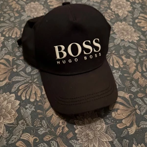 Hugo Boss keps - Tja,   Håller på och rensar min garderob. Denna kepsen kommer inte mer till användning och därav försöker jag sälja den billigt. Kepsen är använd men är hyfsat/okej skick. Stolek - 56, alltså barn storlek. MVH Hugo, vid fler frågor/bilder vänligen hör av dig.