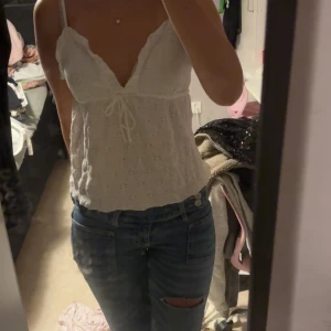 Vit spetsig linnetopp med snörning - Säljer en söt vit linnetopp med spetsdetaljer och broderade blommor. Toppen har v-ringning, smala axelband och en snörning framtill som ger en extra gullig touch. Perfekt för varma dagar och sommarhäng med vänner.