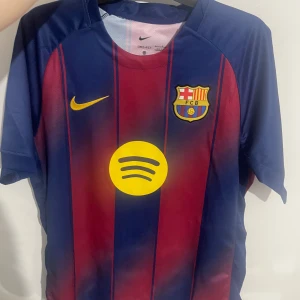 FC Barcelona Pedri L - Säljer en officiell FC Barcelona matchtröja med Pedri och nummer 8 på ryggen. Tröjan är kortärmad, har klassiska blå och röda ränder, gula detaljer och klubbmärke på bröstet. Tillverkad i lätt polyester med Dri-FIT teknologi för bästa komfort.