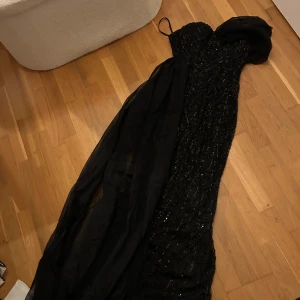 Svart glittrig långklänning - Svart glitttig maxiklänning med ett elegant släp i tunnare tyg. 