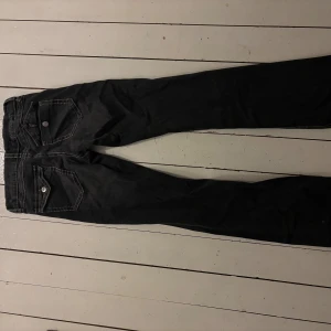 Svarta bootcut jeans med kontrastsömmar - Snygga svarta jeans med vita kontrastsömmar och klassiska fem fickor. Modellen har bootcut-ben och låg midja, vilket ger en cool och avslappnad vibe. Jeansen har silverfärgade knappar och är tillverkade i jeansmaterial.