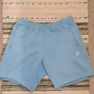 Adidas originals shorts - Säljer ett par knappt använda ljusblåa Adidas mjukisshorts i storlek Large, dom är i nyskick och utan några som helst defekter, fläckar eller pilling..