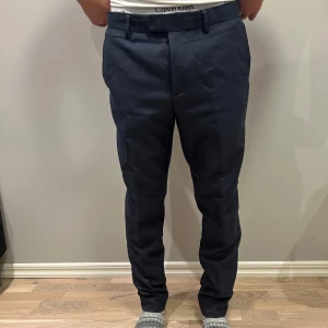 Mörkblå kostymbyxor med raka ben - Snygga mörkblå kostymbyxor med raka ben och klassisk passform. Byxorna har bälteshällor, framfickor och bakfickor med lock och knapp. Materialet känns som en mjuk och slitstark bomullsblandning, perfekt för en stilren look.