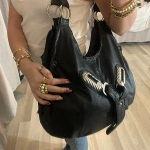 Svart axelväska med silverdetaljer y2k - Fin svart axelväska med silvriga detaljer framtill. Väskan är vintage och har y2k stil.  🫶🏼Säljer pågrund av att jag har många andra väskor som används mer 💞Defekt på ena bandet (bild 3)