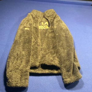 Svart teddyjacka från Superdry - Mjuk och fluffig svart teddyjacka från Superdry Polar i storlek EU 36. Jackan har hel dragkedja framtill, höga krage och två sidofickor med dragkedja. Perfekt för kalla dagar när du vill vara både chill och varm.