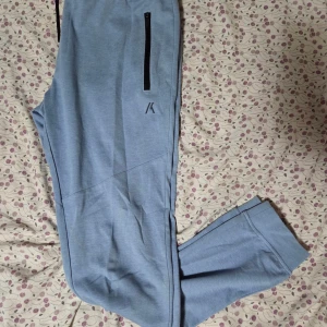 Ljusblå mjukisbyxor  - Snygga ljusblå mjukisbyxor från Produkt med svarta dragkedjor på fickorna och svart snörning i midjan. Byxorna har en relaxed fit och är perfekta för chill dagar. Tillverkade i mjukt bomullsmaterial för extra komfort.