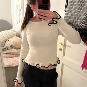 Långärmad topp med volangkant - Supersöt vit långärmad topp med svarta volangdetaljer vid ärmslut och nederkant. Toppen är från ginatricot och i storlek S. Använd fåtal gånger efter köp. Säljer den då jag inte gillar passformen på mig själv!💕💕💕