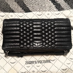 Svart Zadig & Voltaire väska NYPRIS 4000 - Snygg & klassisk Zadig & Voltaire väska i svart äkta läder med silverdetaljer och den ikoniska vingloggan framtill. Väskan kan bäras som en axelväska eller crossbody med justerbar kedjerem! Perfekt för både användning i vardagen och på fest! Dustbagen ingår i priset! Priset kan såklart diskuteras😊