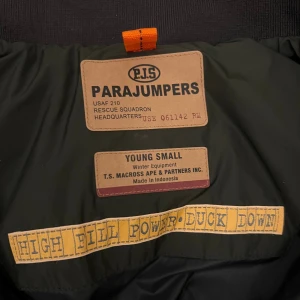 Mörkgrön dunväst från Parajumpers - Snygg mörkgrön dunväst från Parajumpers med hög krage, svarta detaljer och gul rem vid halsen. Västen har quiltad design, dragkedja och knappar framtill. Perfekt för kalla dagar och har en cool, sportig look.