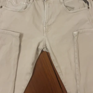 Replay ljusa jeans med raka ben - Snygga ljusbeige jeans från Replay med raka ben och klassiska fem fickor. Byxorna har diskret Replay-logga på bakfickan och stilrena sömmar. Perfekt för dig som gillar enkel och clean stil. Materialet är jeans och midjan är normal.