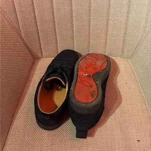 Blåa louboutin med röd sula - Blåa louboutins med snygg röd yttersula och diskret snörning. Ovandelen är i mocka och insidan har en beige skinnklädsel som ger extra komfort. Skorna har en platt sula och rund tå, perfekt för dig som gillar stilrena och coola detaljer.