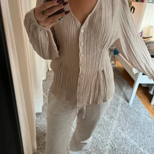 Beige plisserad skjorta från Lindex - Säljer en beige plisserad skjorta från Lindex med v-ringning och långa ärmar. 