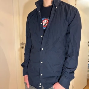 Mörkblå skjorta med knappar - Snygg mörkblå skjorta med klassisk krage och vita knappar hela vägen. Skjortan har lång ärm och en stilren, enkel design som passar till jeans eller chinos. Tillverkad i bomull för en skön känsla och bra passform. Passar om du är 175cm+