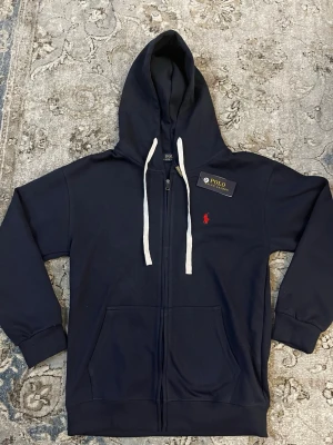 Ralph Lauren zip - Detta är en mörkblå zip up tröja från Ralph lauren, tröjan är helt ny och det finns även taggen kvar och självaste Raulph lauren påsen. Det står M men jag skulle ganska säkert säga att det passar som en S.