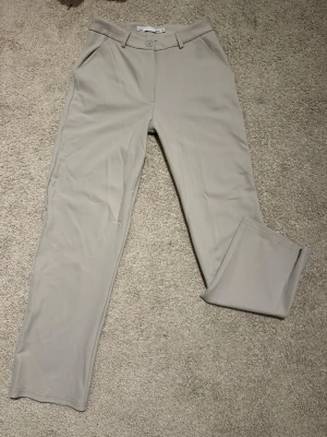 Grå kostymbyxor – XS – stilrena och bekväma - Eleganta beige kostymbyxor i storlek XS med tidlös design. Modellen är midwaist, raka ben och bälteshällor som ger en stilren siluett. Tyget är mjukt men håller formen fint, vilket gör dem bekväma att bära hela dagen.✨  Passar perfekt till både vardag och mer uppklädda tillfällen🩷