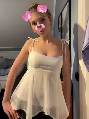 Vit ärmlös linnetopp med knyt - Supersöt vit linnetopp med tunna axelband som knyts på axlarna. Toppen har en flowy, lätt utsvängd passform och är gjord i ett tunt, luftigt material som känns perfekt för varma dagar. Enkel men ändå riktigt fin detalj med knytbanden.