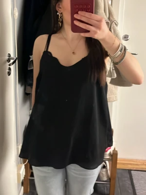 Svart linnetopp  - Säljer en svart linnetopp från Cubus i storlek 36. Toppen har tunna axelband och en lös passform med lätt v-ringad halsringning. Materialet känns mjukt och svalt mot huden. 💞