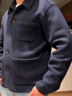 Mörkblå overshirt från Polo Ralph Lauren - Säljer en mörkblå overshirt från Polo Ralph Lauren i ull. Jackan har tre stora fickor framtill, knäppning med svarta knappar och klassisk krage. Perfekt för lager-på-lager och riktigt snygg till jeans eller chinos. Den har tyvärr råkat hamna med i tvätten så den har blivit en small. Men den är fortfarande i ett väldigt bra skick nästa intill perfekt. Ny pris 4295 kr